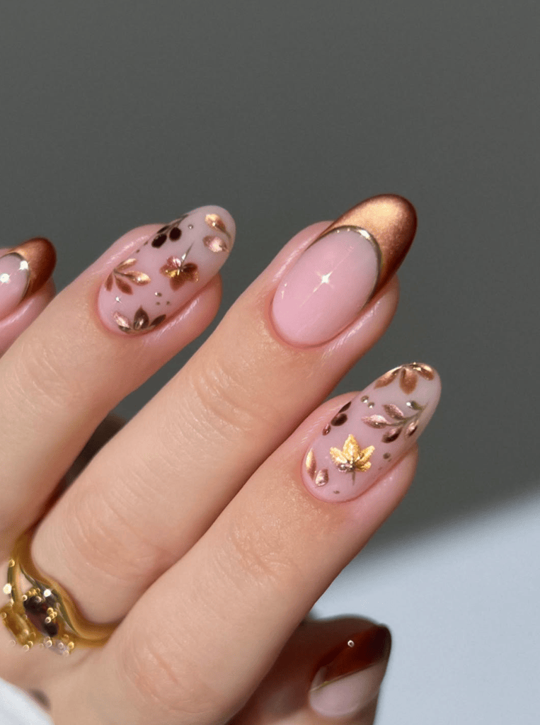 Close-up of elegantly manicured nails featuring a light pink base with gold leaf designs and a shiny metallic brown tip, highlighted by a delicate gold accent.
