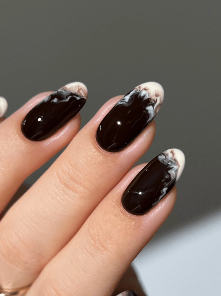 Close-up of manicured nails featuring a chocolate brown base with marble-like white and creamy patterns on the tips.