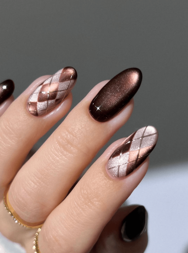 A close-up of a hand showcasing stylish nail art featuring a combination of brown and metallic colors with diamond patterns and glossy finishes.