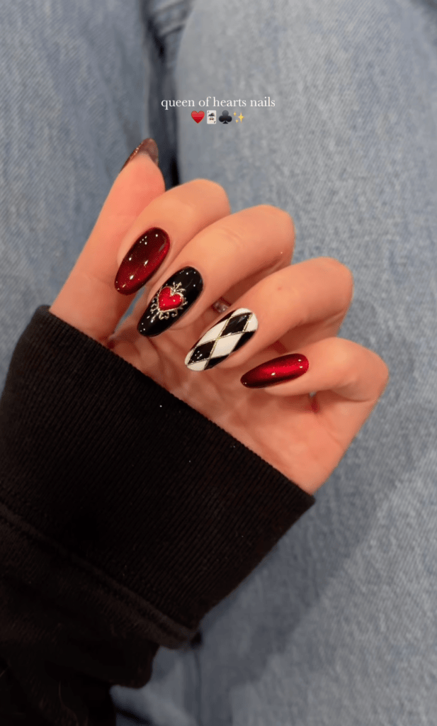 Close-up of stylish nail art featuring a mix of red and black colors, including a heart design and a diamond pattern, on a hand against a denim background.