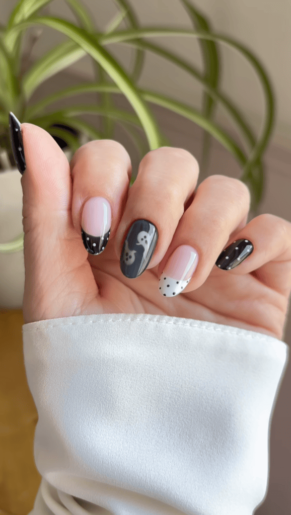 A close-up of a woman's hand displaying nail art, featuring a mix of black, white, and pink colors, with designs including polka dots and a skull motif.