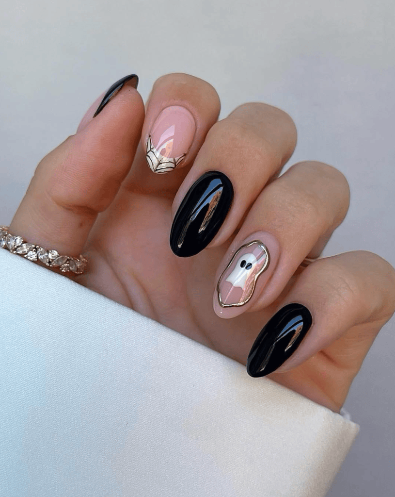 Close-up of a manicured hand with black and pink nails, featuring a ghost design on one nail and a gold geometric pattern on another.