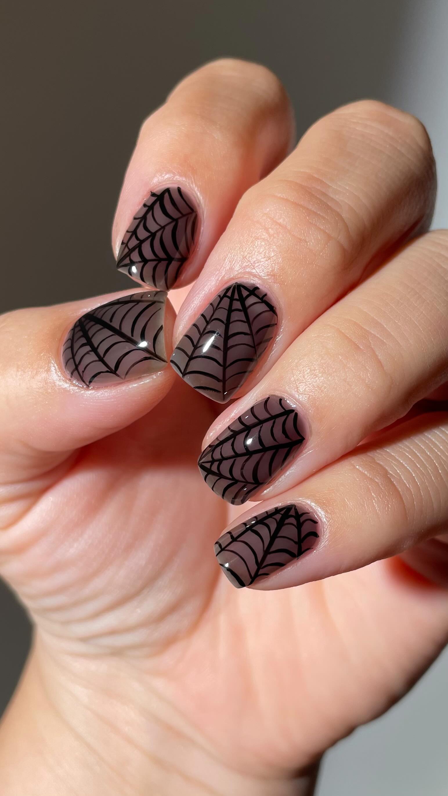 A hand displaying beautifully manicured nails with a spider web design in black on a nude background.