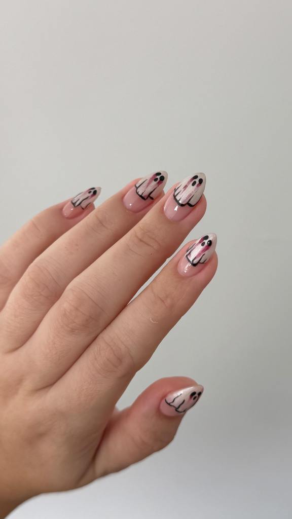 A hand displaying a manicure with ghost designs on the nails, featuring a pink base and black and white details.