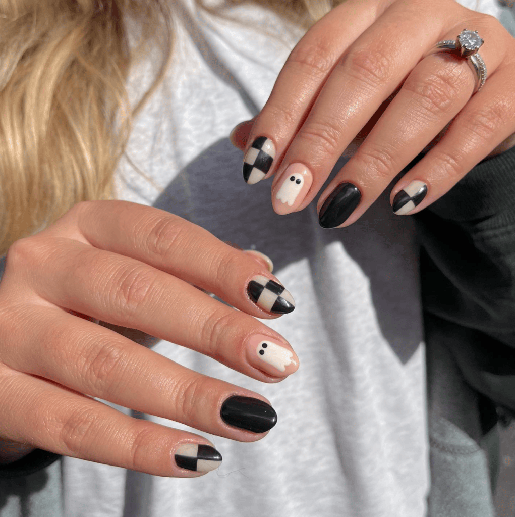 Close-up of a woman's hands with Halloween-themed nail art featuring black, white, and checkered patterns, including a cute ghost design.